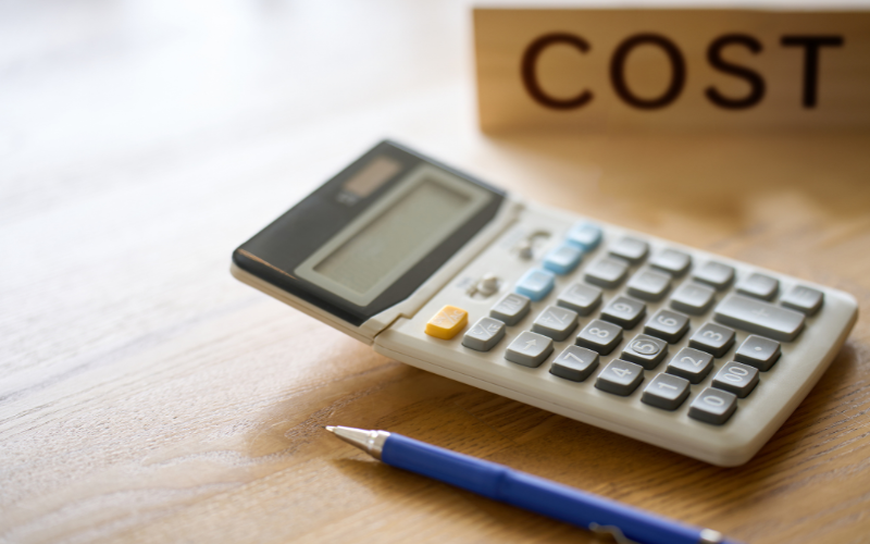 Calculator and pen on a table with cost sign behind